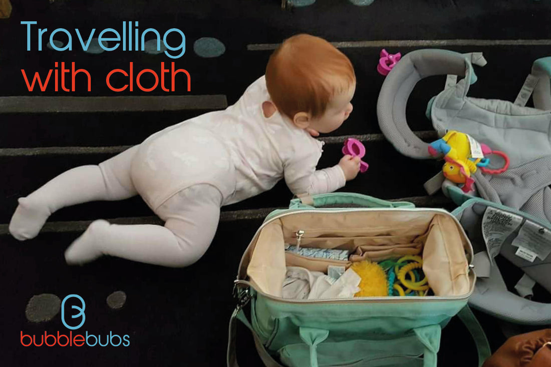 Baby-on-the-floor-with-a-pink-onesie-and-a-nappy-bag-and-baby-carrier