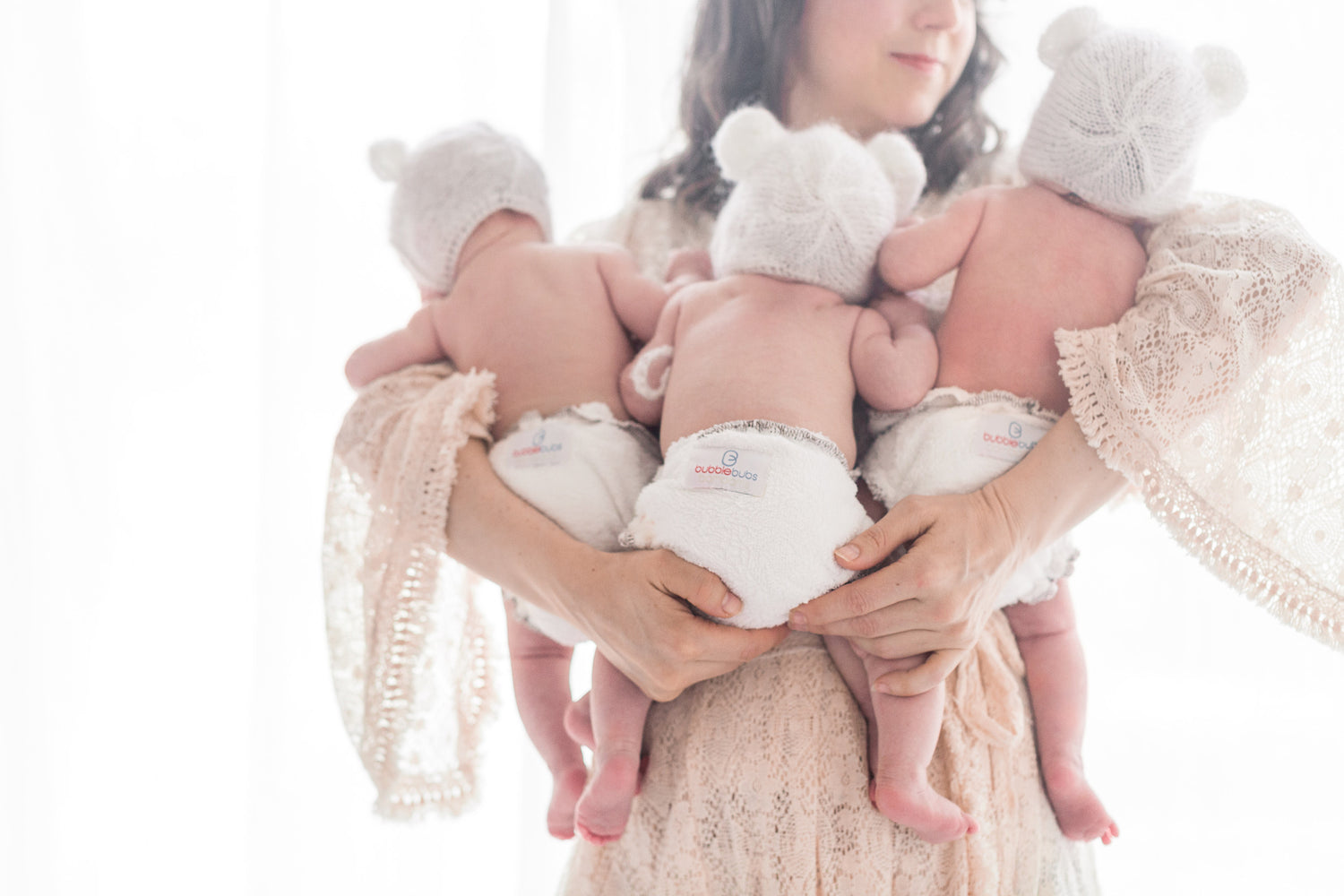 Mother holding three babies all waring Bambam cloth nappies without PUL covers done up with a snappi.