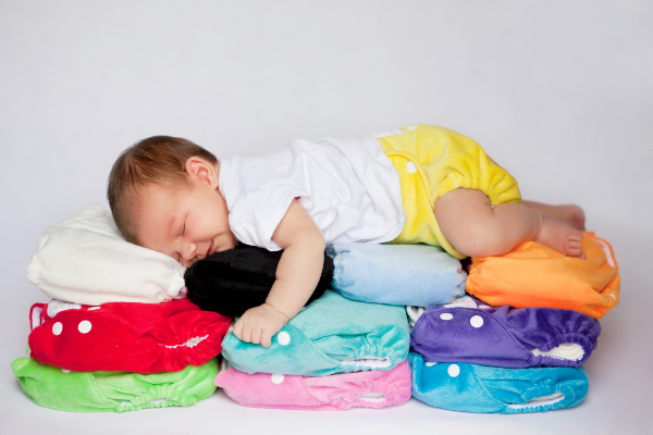 sleeping baby laying on a bed of cloth nappies waring a yellow cloth nappy