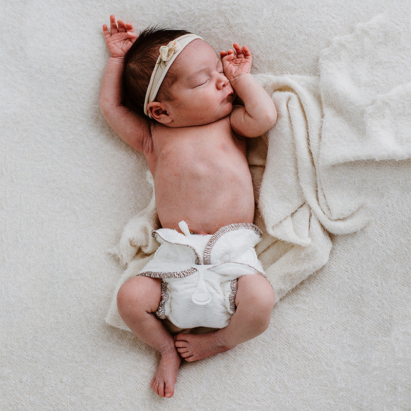 bambam cloth nappy on a sleeping newborn baby. on a soft white background with a snapi doing the cloth nappy up