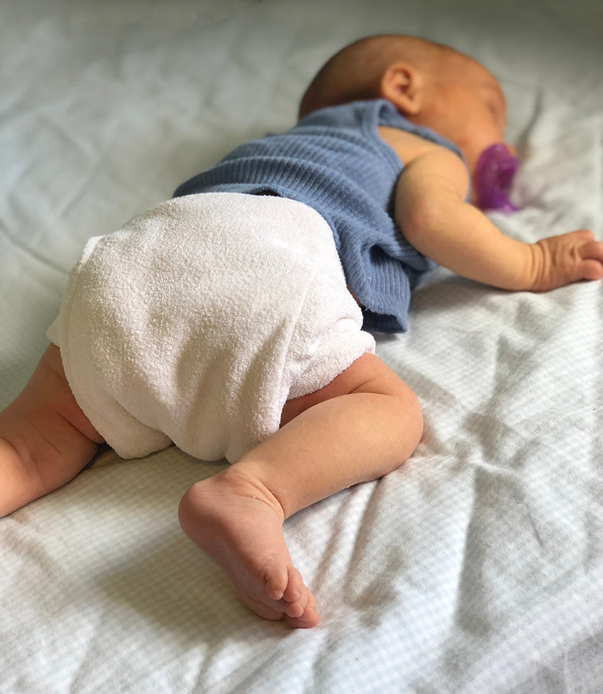 Newborn baby wearing prefold cloth nappy, lying on a blanket.
