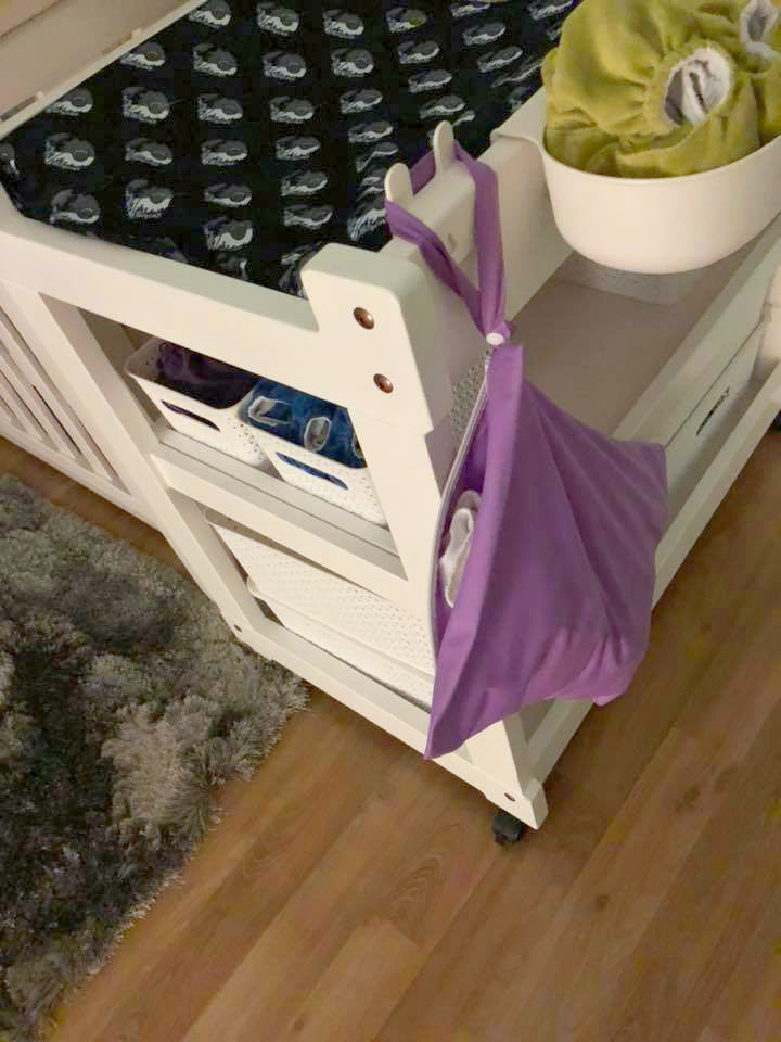 Purple wetbag hanging off a baby's change table.