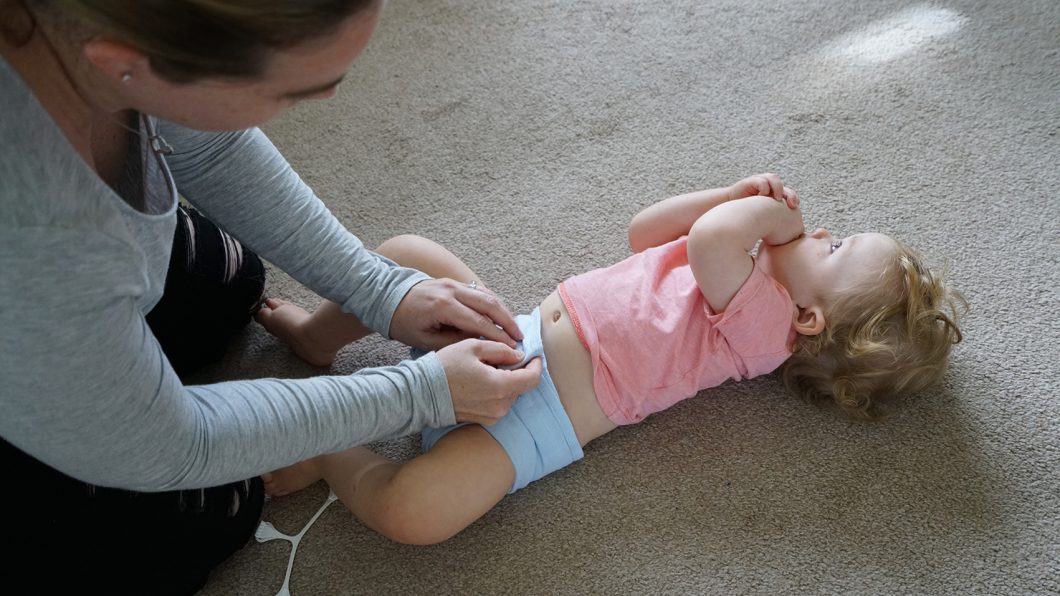 A mum changing a baby's muslin flat cloth nappy on the floor.