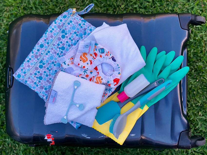 Suitcase, on grass with accessories for travelling with cloth nappies on top.