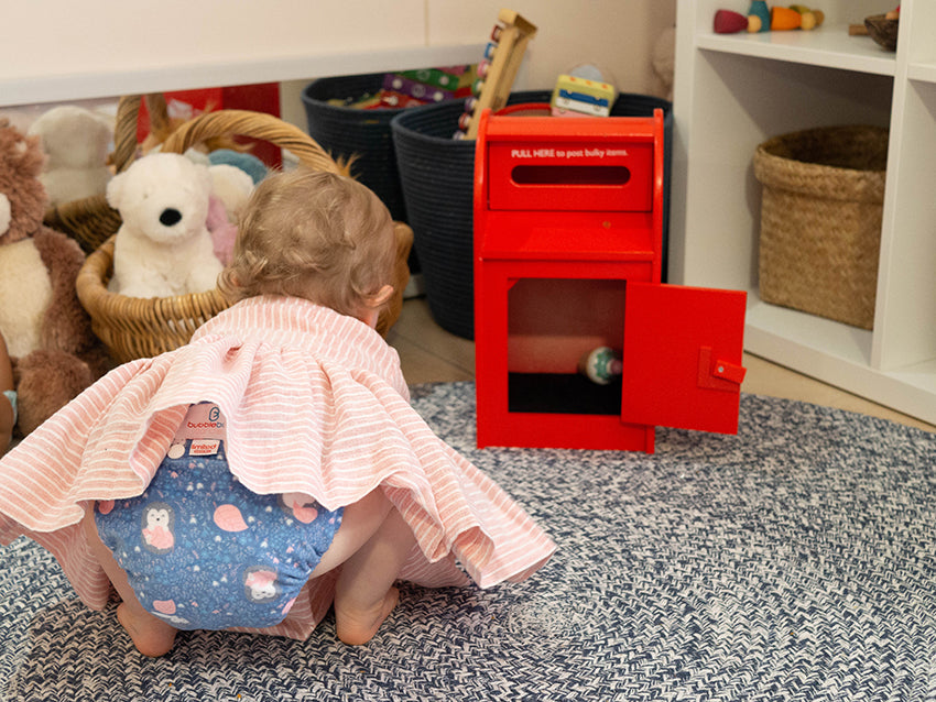 Toddler reaching for toy blue and pink modern cloth nappy poking out from underneath.