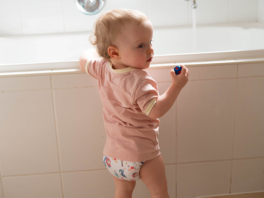 Toddler standing in front of a bath wearing an all in two cloth nappy