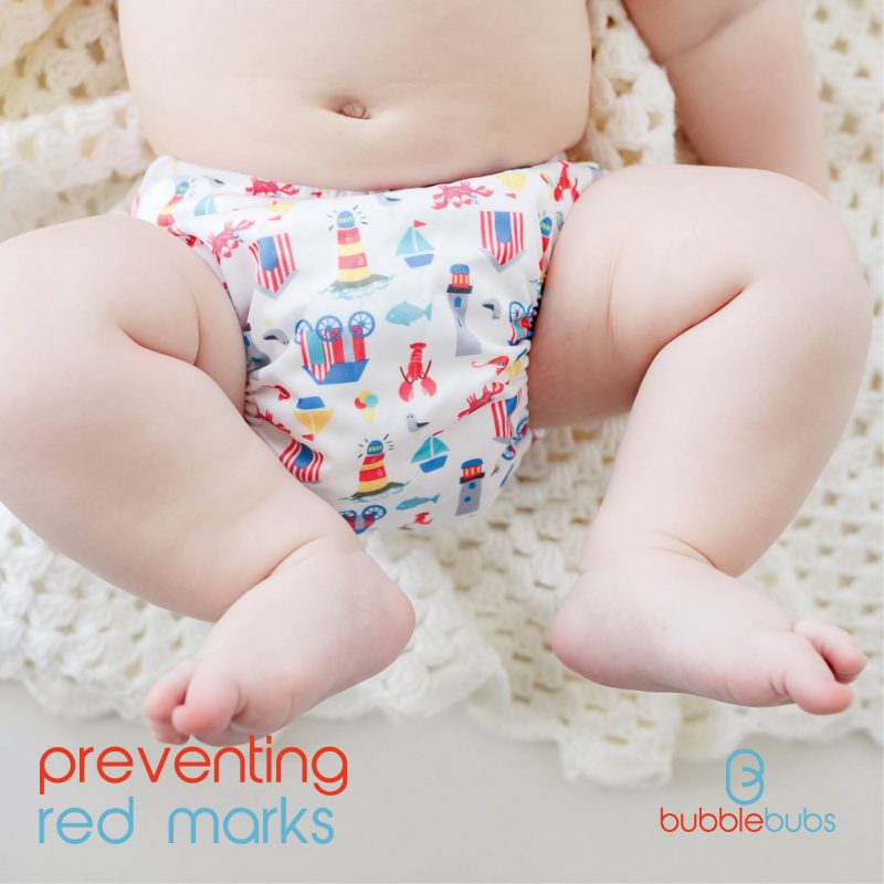 Lower-torso-of-baby-wearing-cloth-nappy-with-seaside-icons-laying-on-cream-blanket
