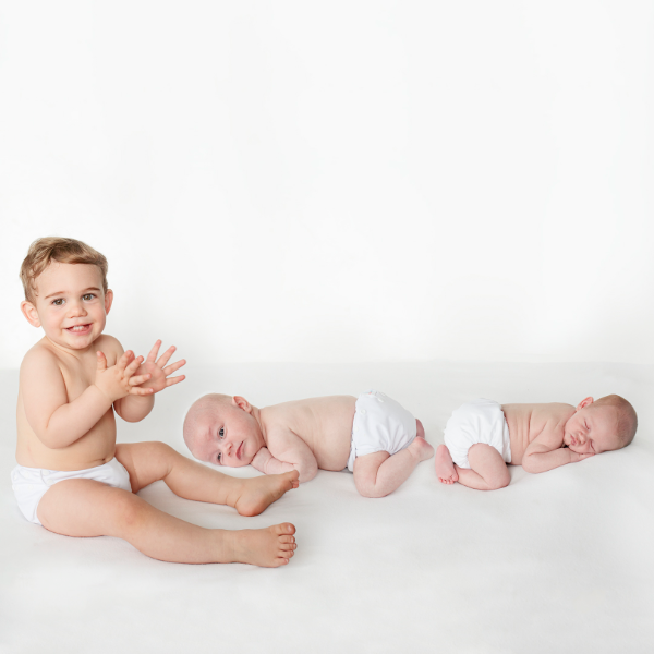 a newborn infant and toddler waring white candie cloth nappies on a white background