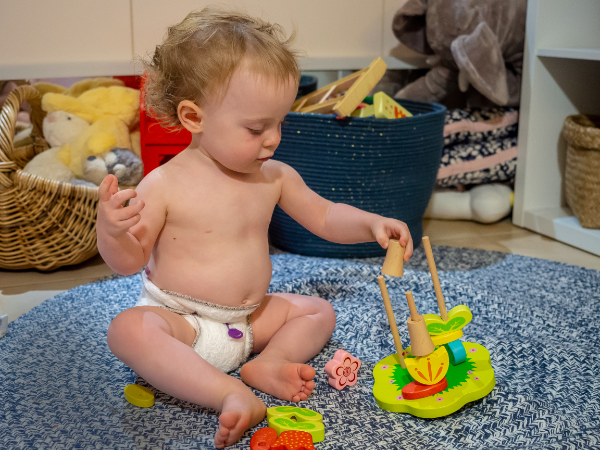 one year old baby playing with a top waring Bambam newborn cloth nappy white with red snappi