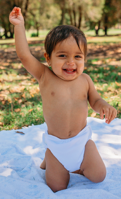 happy baby with one hand in the air waring a white cloth nappy candie
