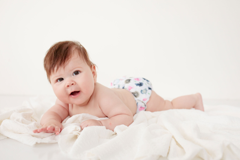 Baby looking at you on a blanket waring a cloth nappy