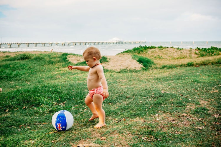 a toddler in a pink candie cloth nappy at the beach playing with a beach ball 