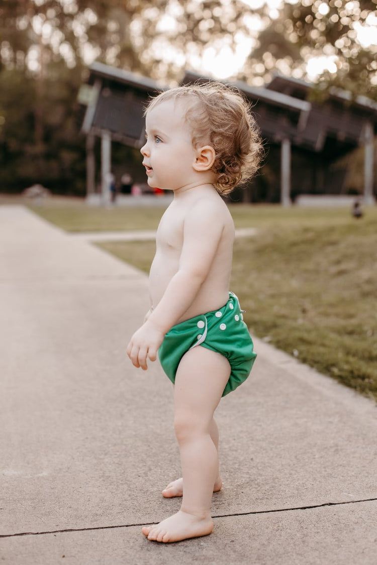 toddler in a green cloth nappy on a path at a park